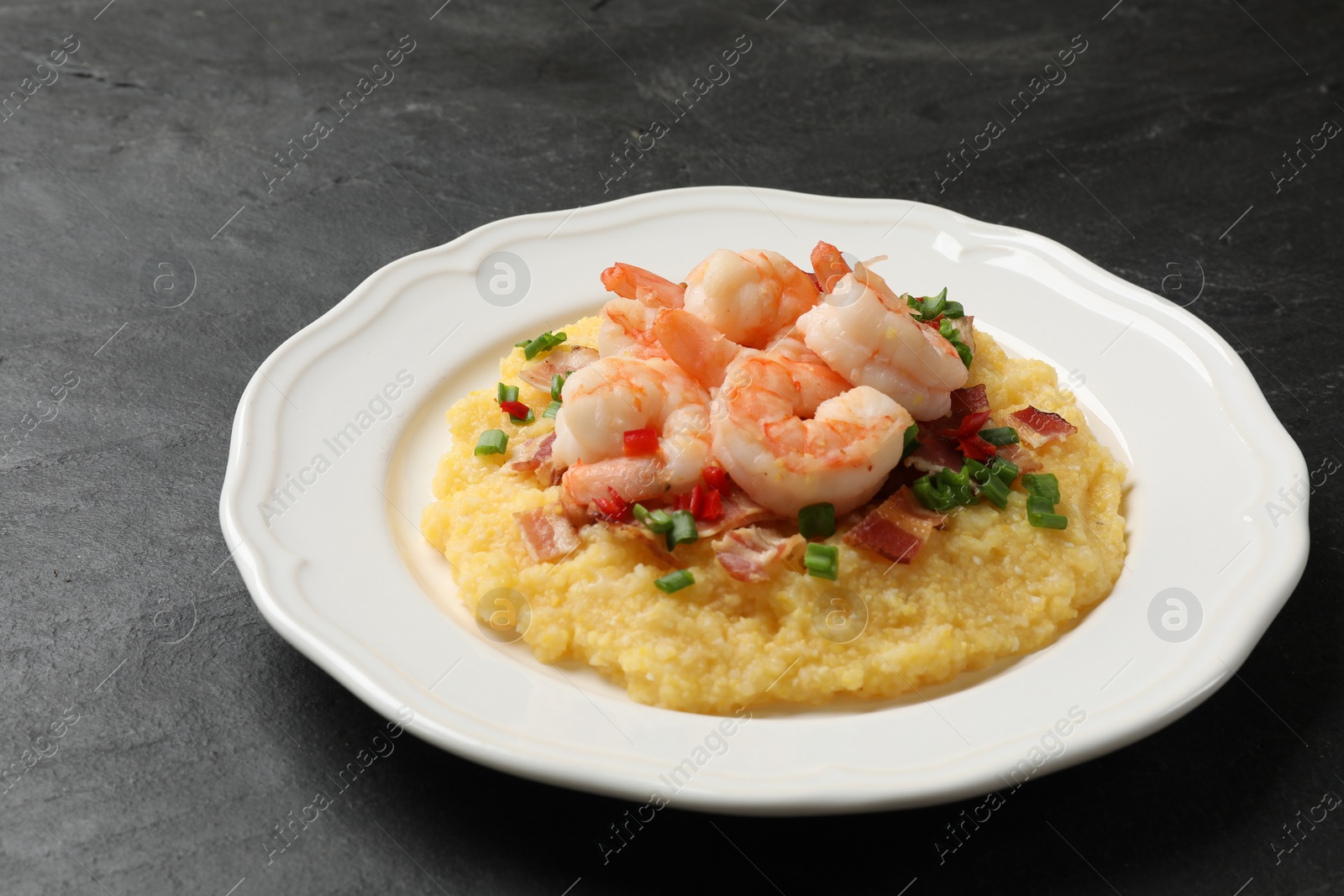 Photo of Plate with fresh tasty shrimps, bacon, grits, green onion and pepper on black table, closeup