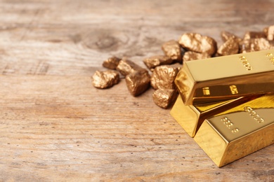 Gold nuggets and ingots on wooden background. Space for text