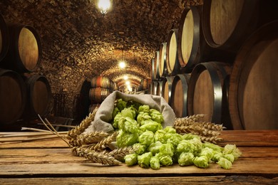Fresh hops and wheat spikes on wooden table in beer cellar