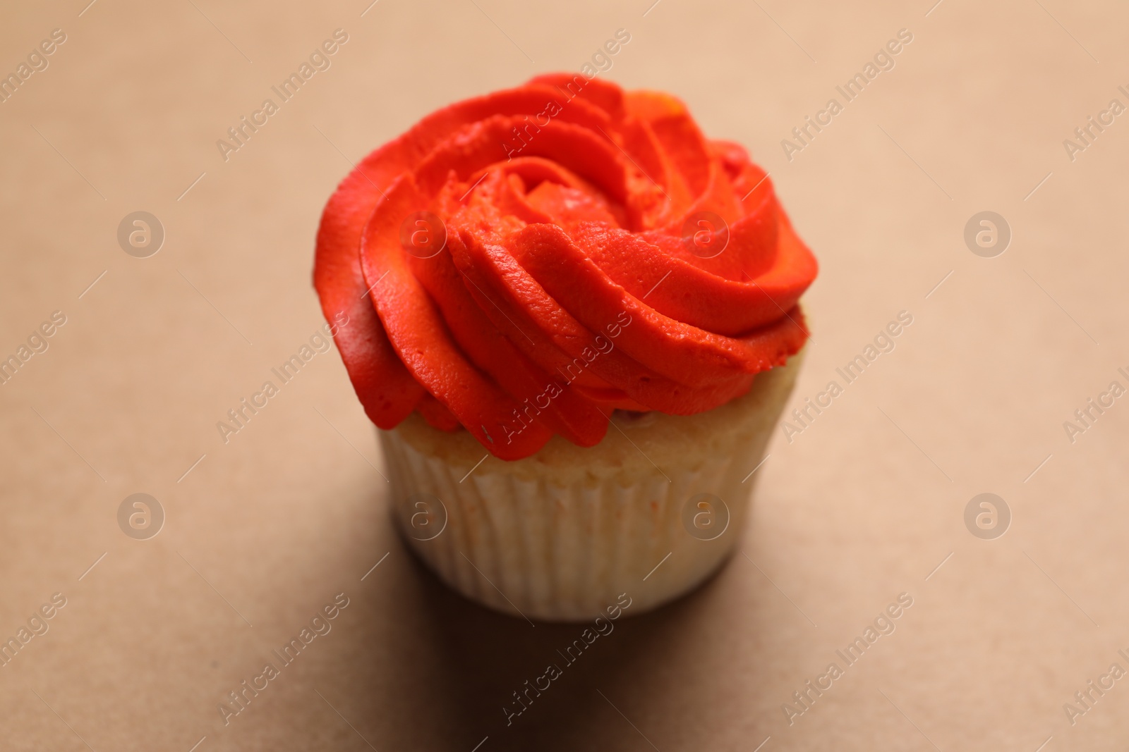 Photo of Delicious cupcake with bright cream on brown background, closeup