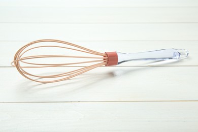 Photo of One whisk on white wooden table, closeup