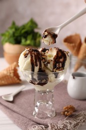 Eating tasty ice cream with chocolate topping and nuts at table