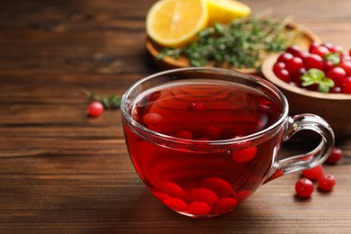 Photo of Tasty hot cranberry tea in glass cup and fresh berries on wooden table