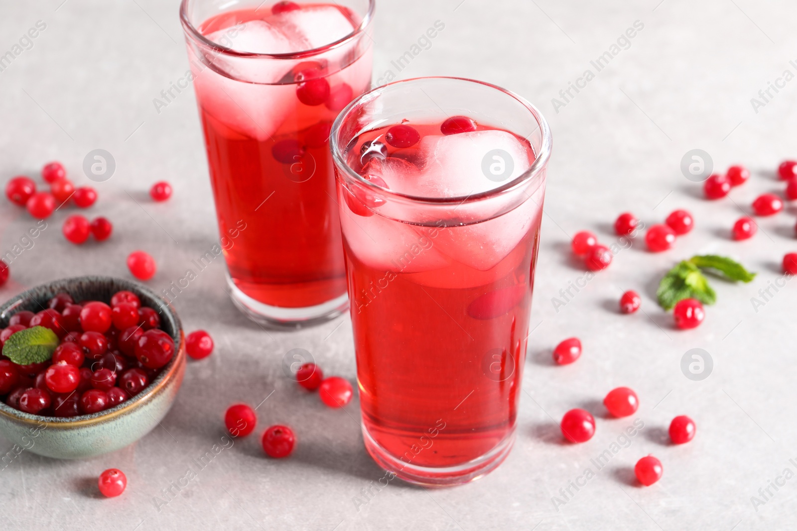 Photo of Tasty cranberry juice with ice cubes in glasses and fresh berries on light grey table, closeup
