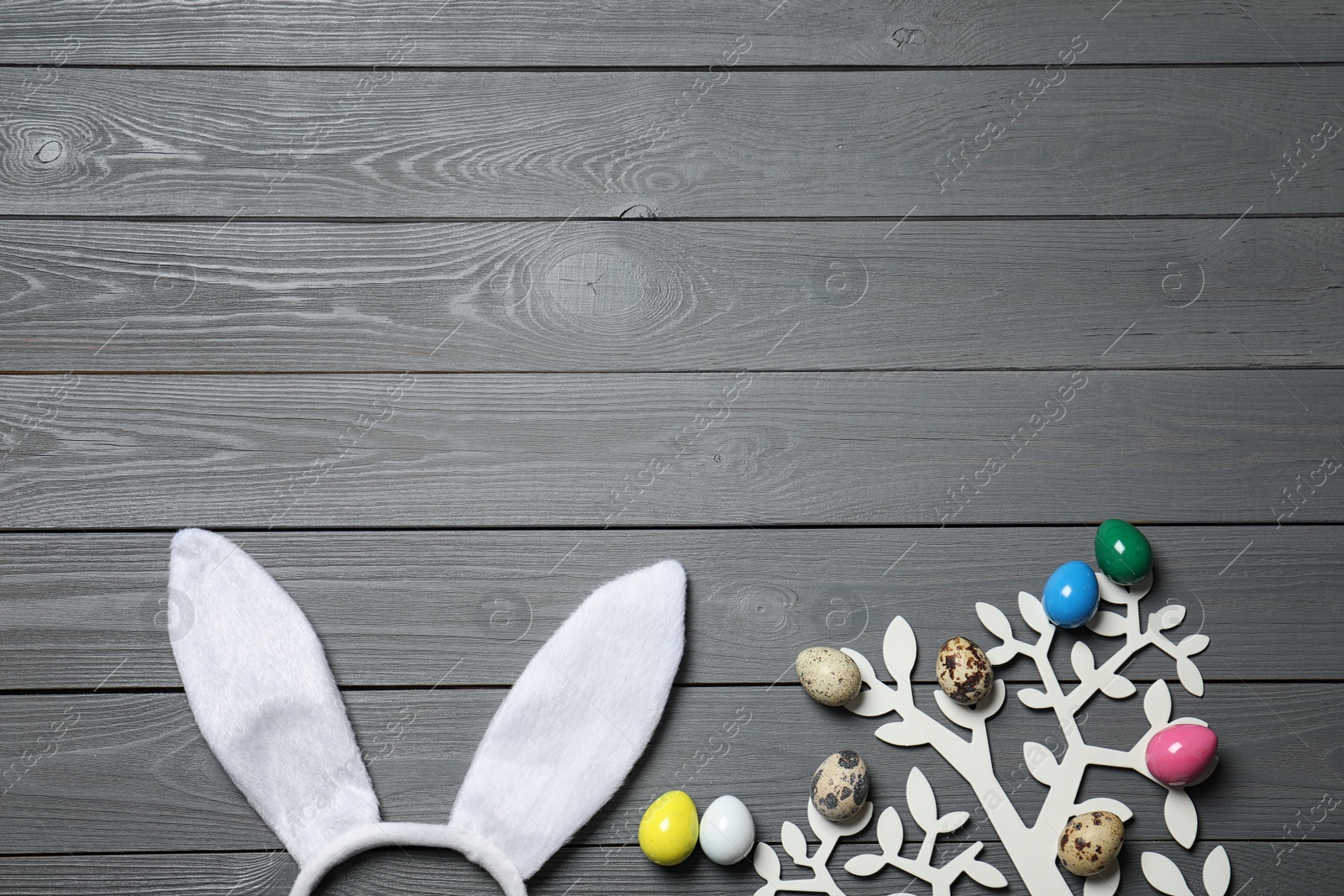 Photo of Easter bunny ears headband and decorative tree with colorful eggs on wooden background, flat lay. Space for text