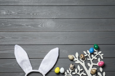 Photo of Easter bunny ears headband and decorative tree with colorful eggs on wooden background, flat lay. Space for text