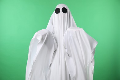 Photo of Creepy ghost. Person covered with white sheet on green background