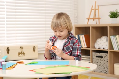 Photo of Cute little boy using glue stick at desk in room. Home workplace