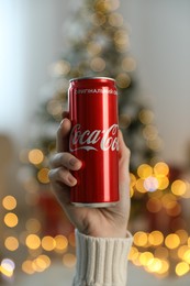 MYKOLAIV, UKRAINE - January 01, 2021: Woman with can of Coca-Cola against blurred Christmas tree indoors, closeup