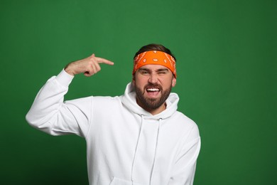 Fashionable young man in stylish outfit with bandana on green background