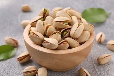 Photo of Delicious pistachios in bowl on grey textured table, closeup