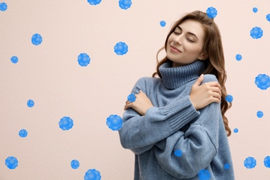 Image of Stronger immunity - better disease resistance. Young woman in warm blue sweater surrounded by viruses on beige background