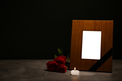 Empty frame with black ribbon, candle and roses on table. Funeral symbol