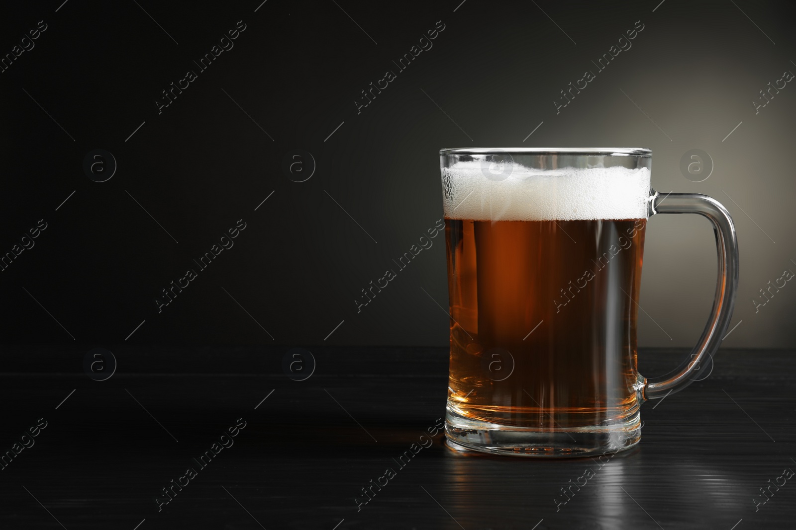 Photo of Glass mug with cold tasty beer on dark background