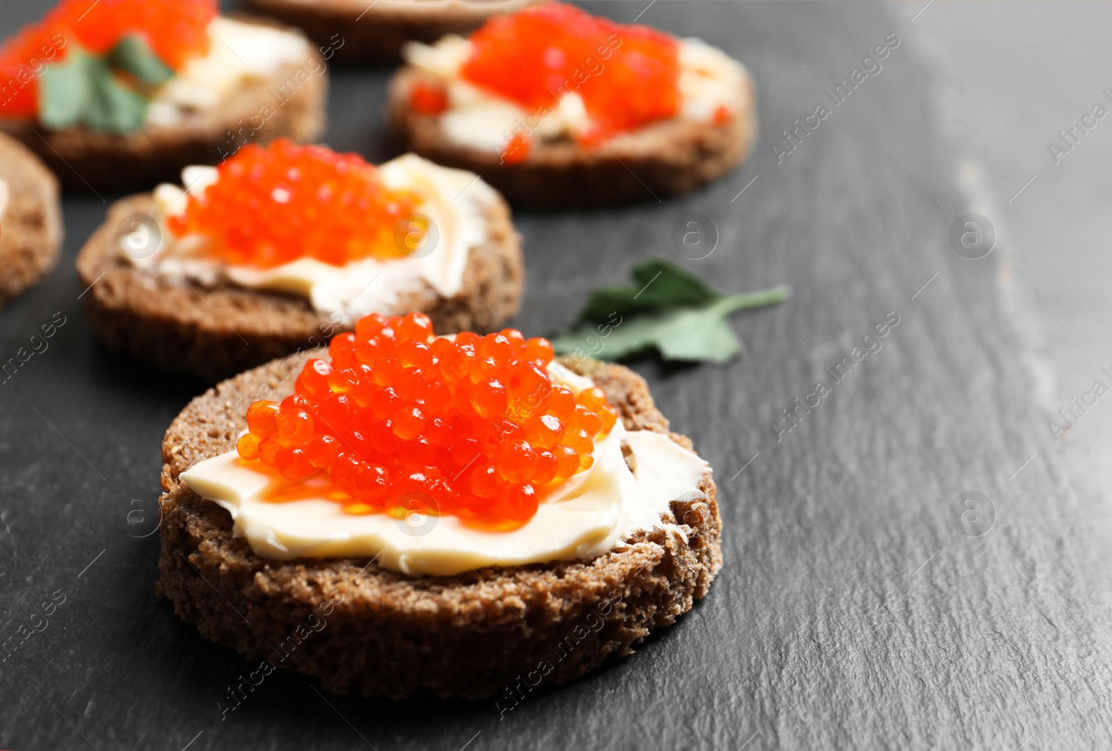 Photo of Delicious sandwiches with red caviar on slate plate