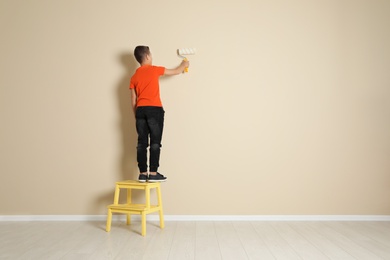 Photo of Child on step chair painting color wall with roller brush. Space for text