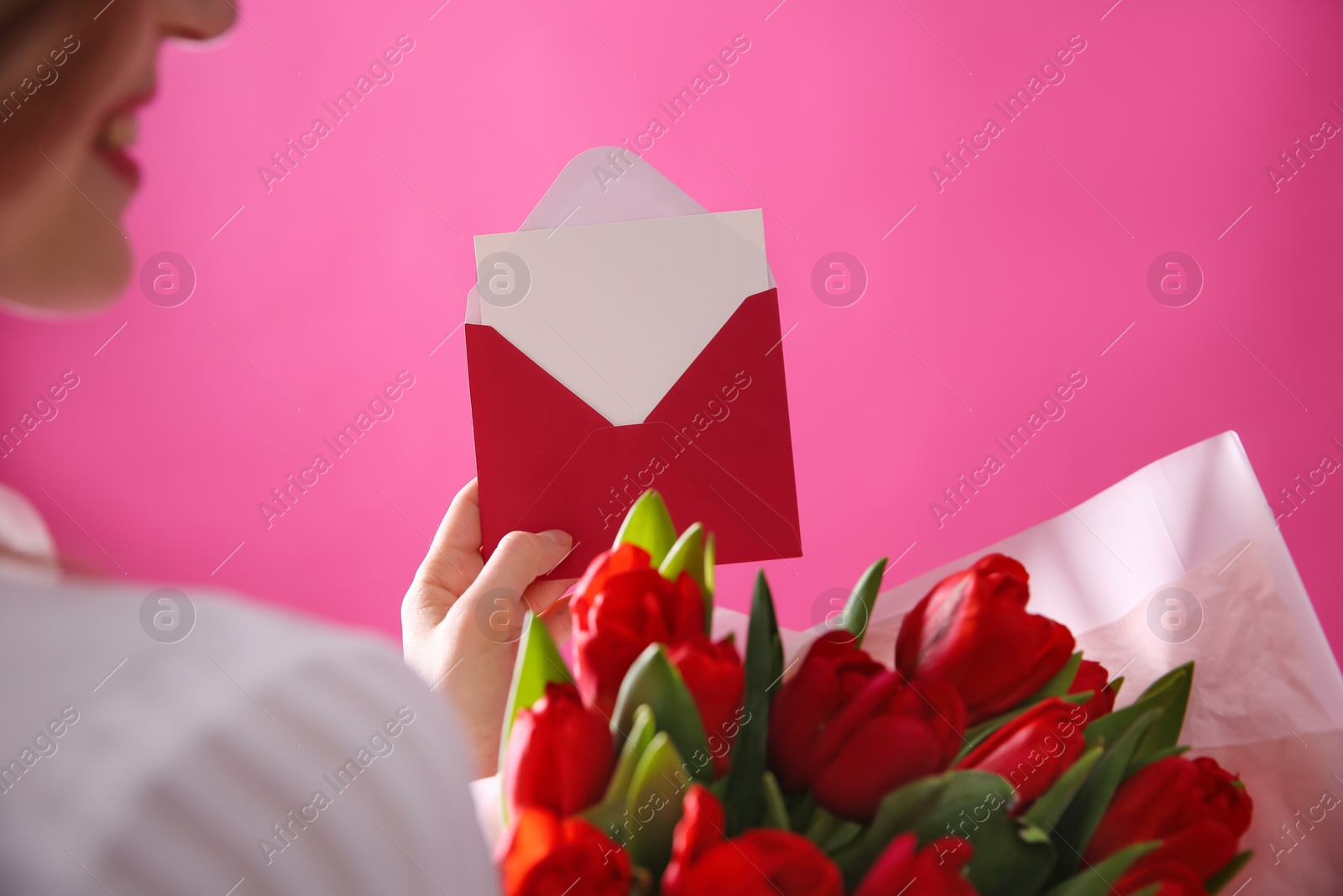 Photo of Woman holding envelope with blank greeting card and bouquet of tulips on pink background, closeup