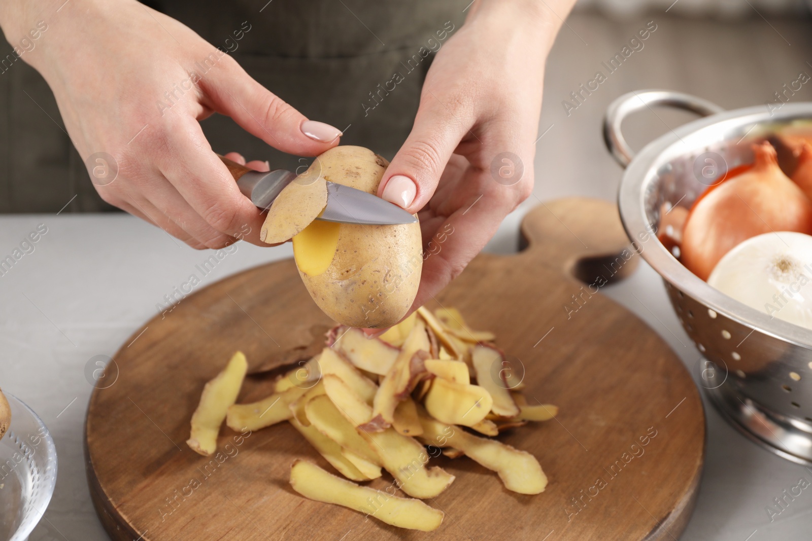 Photo of Woman peeling fresh potato with knife at light table indoors, closeup