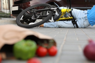 Photo of Woman fallen from bicycle after car accident and scattered vegetables on street
