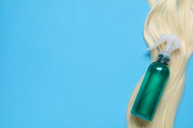 Photo of Spray bottle with thermal protection and lockblonde hair on light blue background, flat lay. Space for text