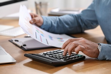 Professional accountant using calculator at wooden desk, closeup