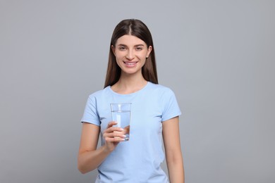 Healthy habit. Portrait of happy woman holding glass with fresh water on grey background