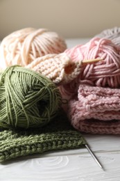 Photo of Balls of soft yarns, knitting and needles on white wooden table