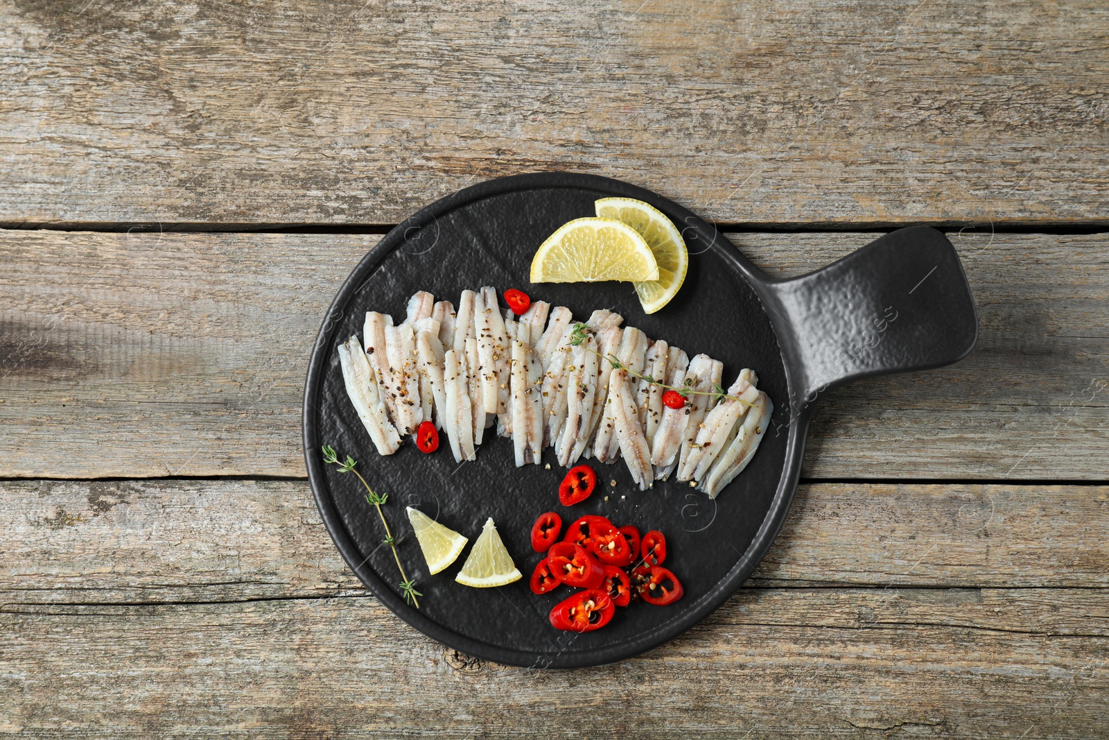 Photo of Tasty anchovies with spices and lemon slices on wooden table, top view