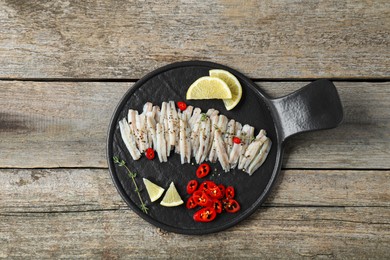 Tasty anchovies with spices and lemon slices on wooden table, top view