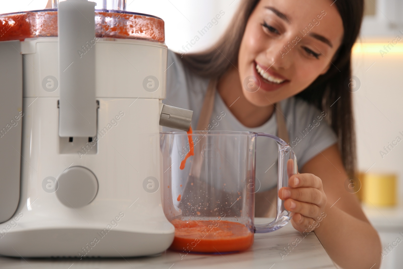 Photo of Young woman making tasty fresh juice at table in kitchen, closeup