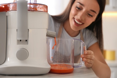 Young woman making tasty fresh juice at table in kitchen, closeup