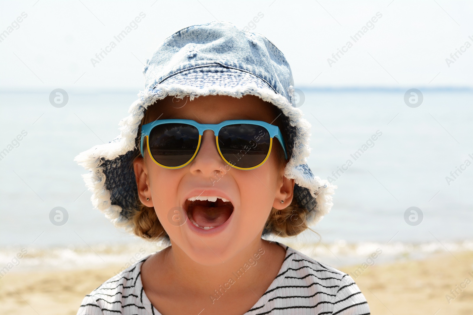 Photo of Little girl wearing sunglasses and hat at beach on sunny day