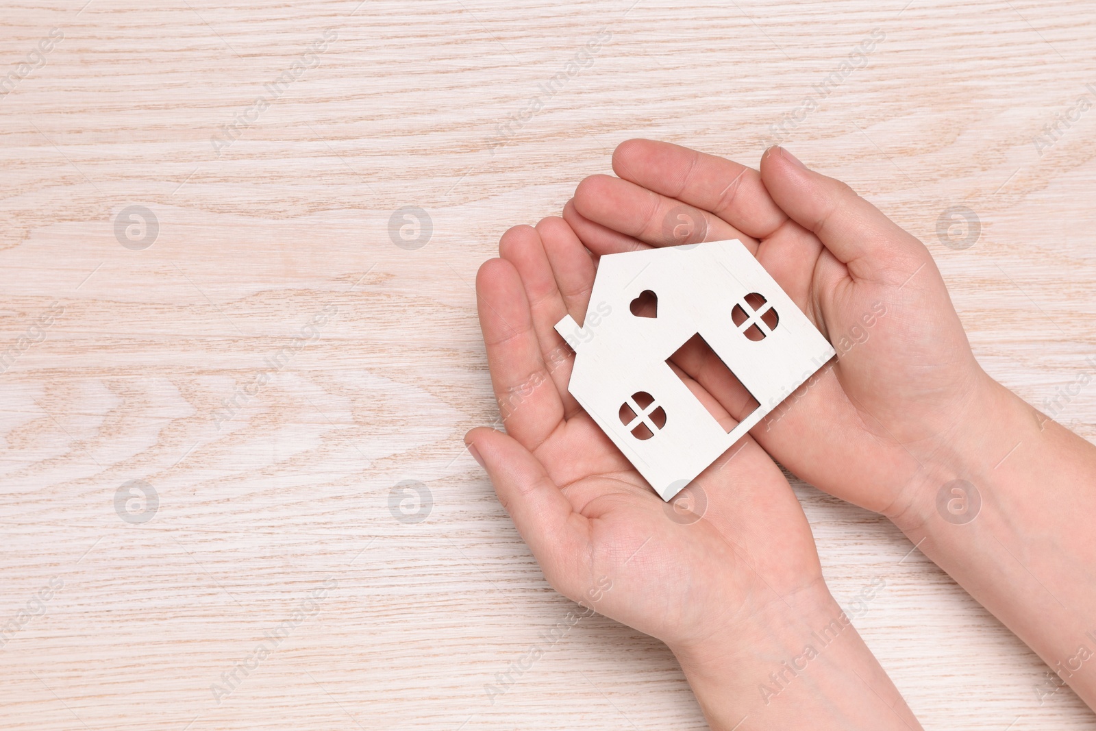 Photo of Home security concept. Man holding house model at wooden table, top view with space for text