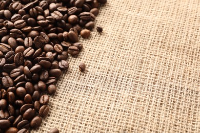 Many coffee beans on burlap fabric, closeup. Space for text