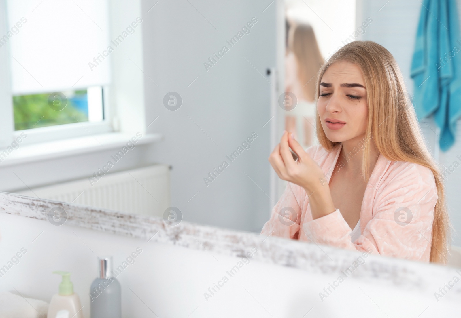 Photo of Young woman with eyelash loss problem looking in mirror indoors