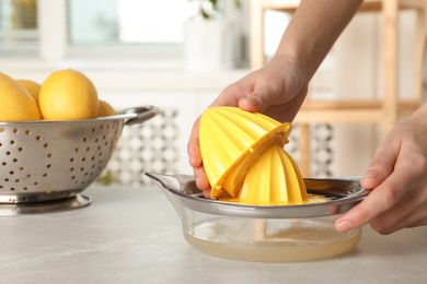 Photo of Woman squeezing lemon juice with reamer at table