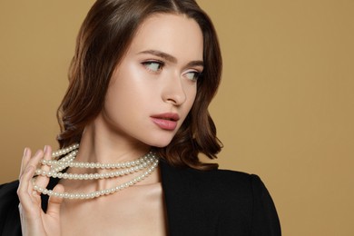 Young woman with elegant pearl necklace on brown background, space for text