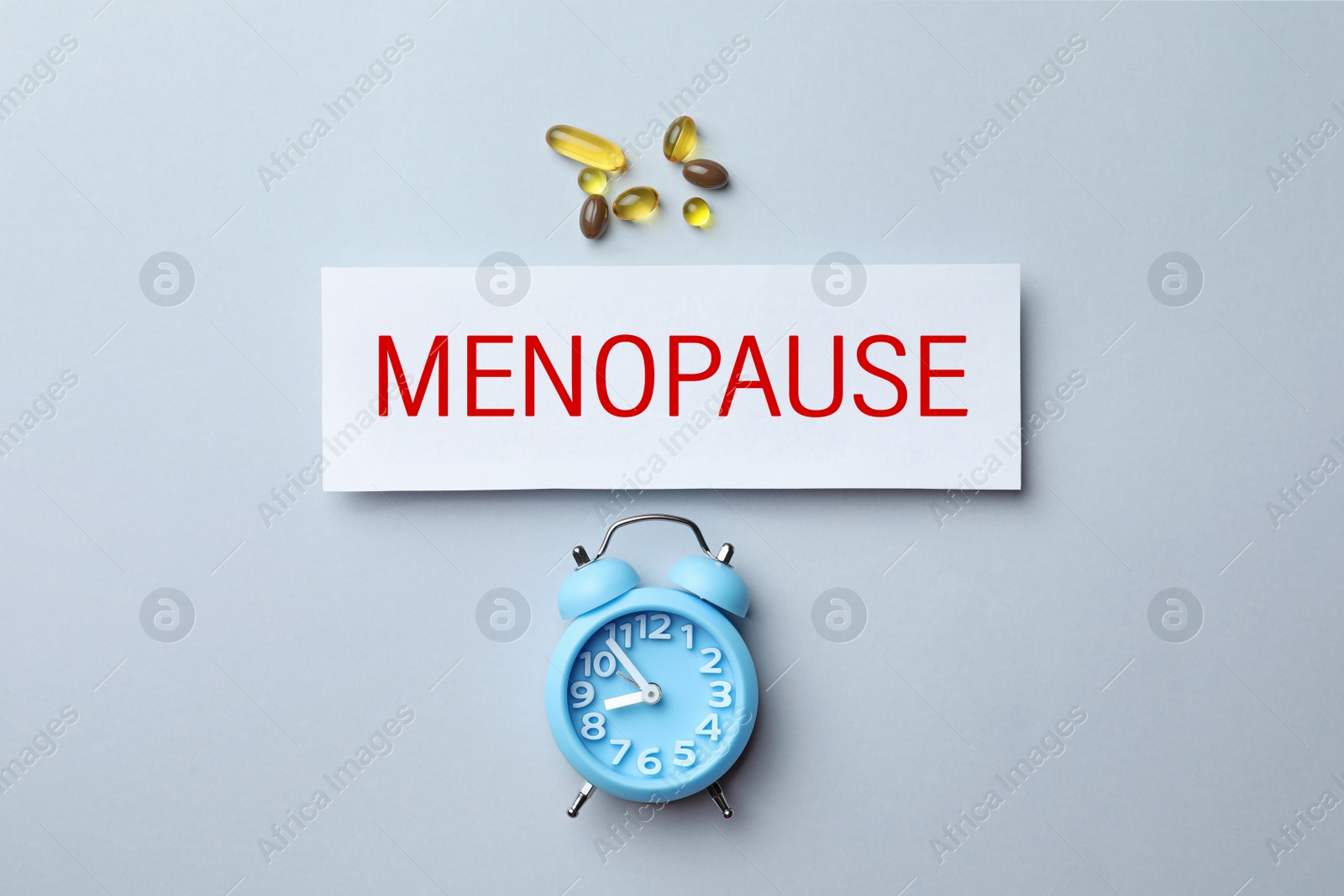 Photo of Card with word Menopause, pills and alarm clock on white background, flat lay