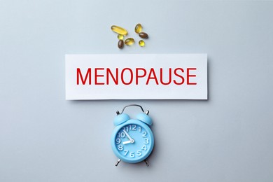 Card with word Menopause, pills and alarm clock on white background, flat lay