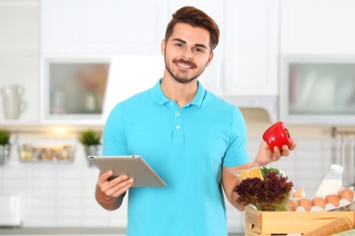 Photo of Young man with tablet PC and products in kitchen. Food delivery service