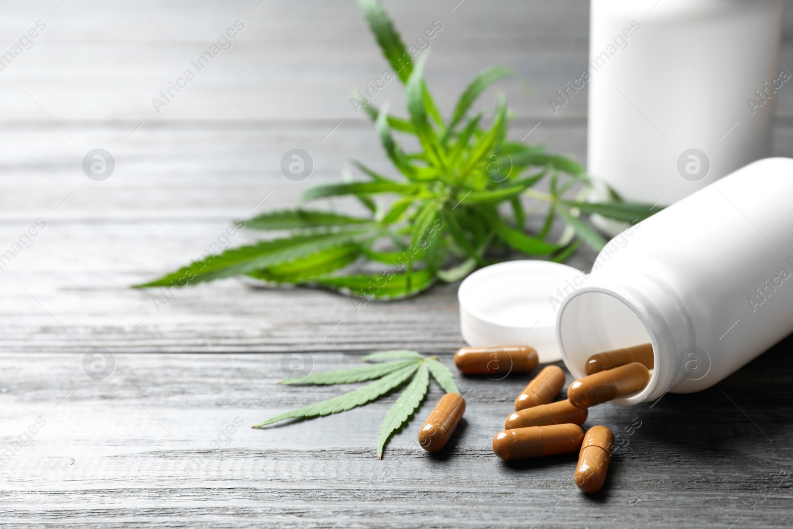 Photo of Hemp leaves and bottle with capsules on grey wooden table. Space for text