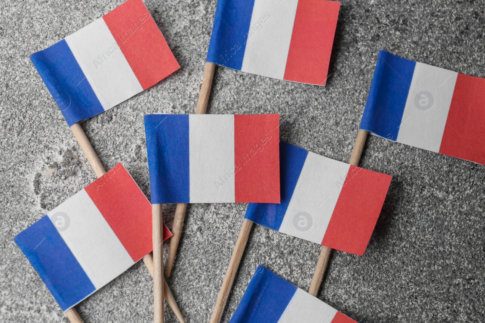 Photo of Small paper flags of France on grey table, flat lay