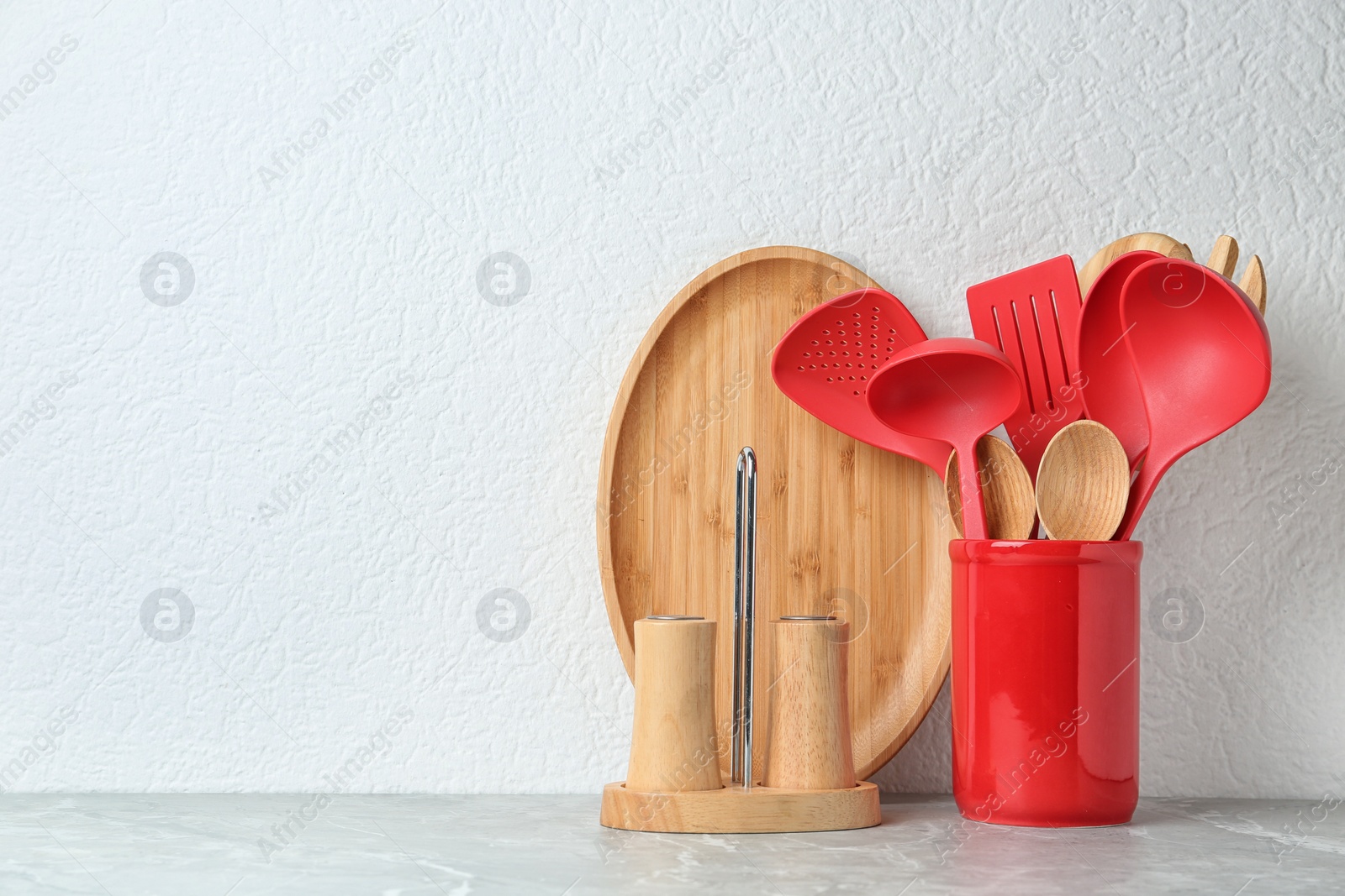 Photo of Set of kitchen utensils in stand on stone table near light wall. Space for text