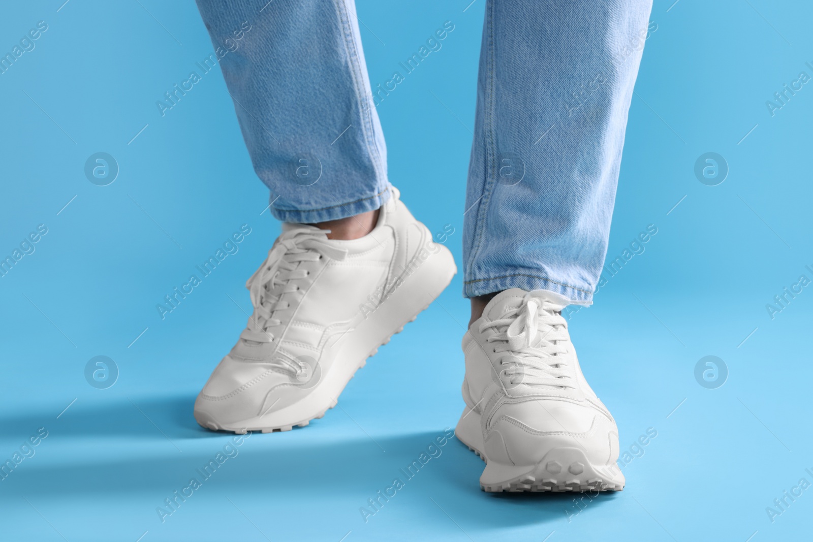 Photo of Man walking in stylish sneakers on light blue background, closeup