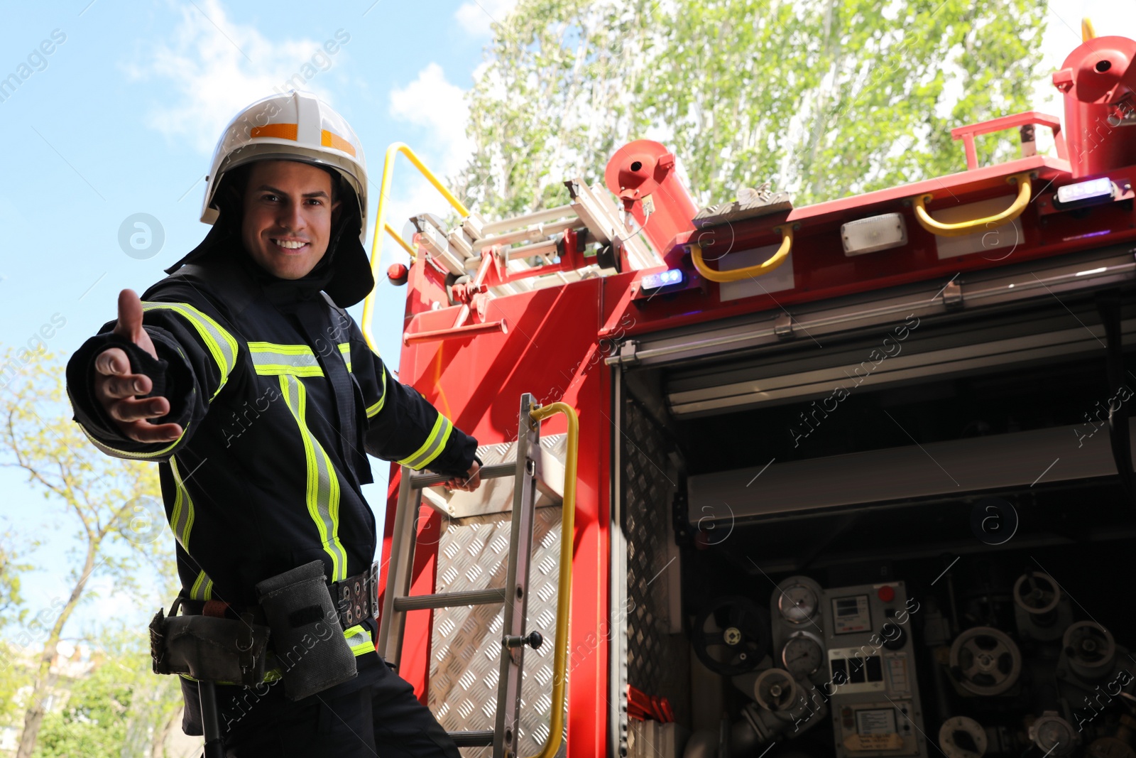 Photo of Firefighter in uniform and helmet offering hand near fire truck outdoors