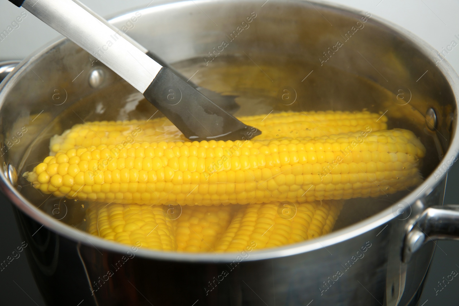 Photo of Taking fresh corn cob from pot with hot water on stove
