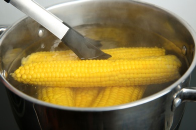 Photo of Taking fresh corn cob from pot with hot water on stove