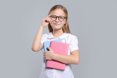 Photo of Portrait of cute girl in glasses with books on light grey background