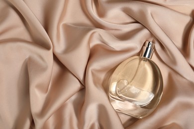 Photo of Luxury perfume in bottle on beige silk fabric, top view