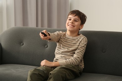 Happy boy changing TV channels with remote control on sofa at home